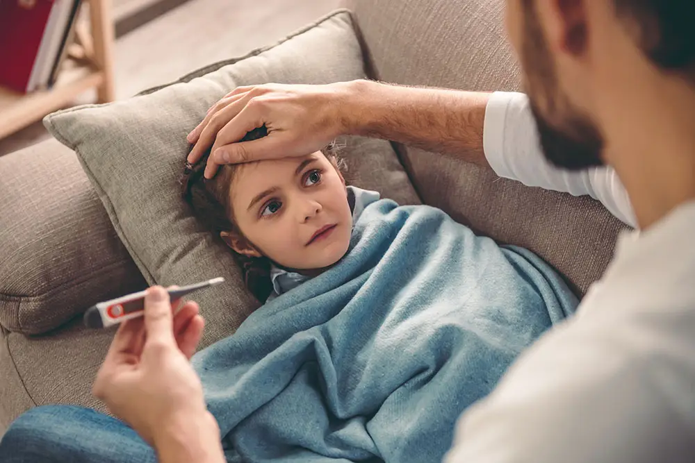 Young girl laying in bed with the flu as her father takes her temperature