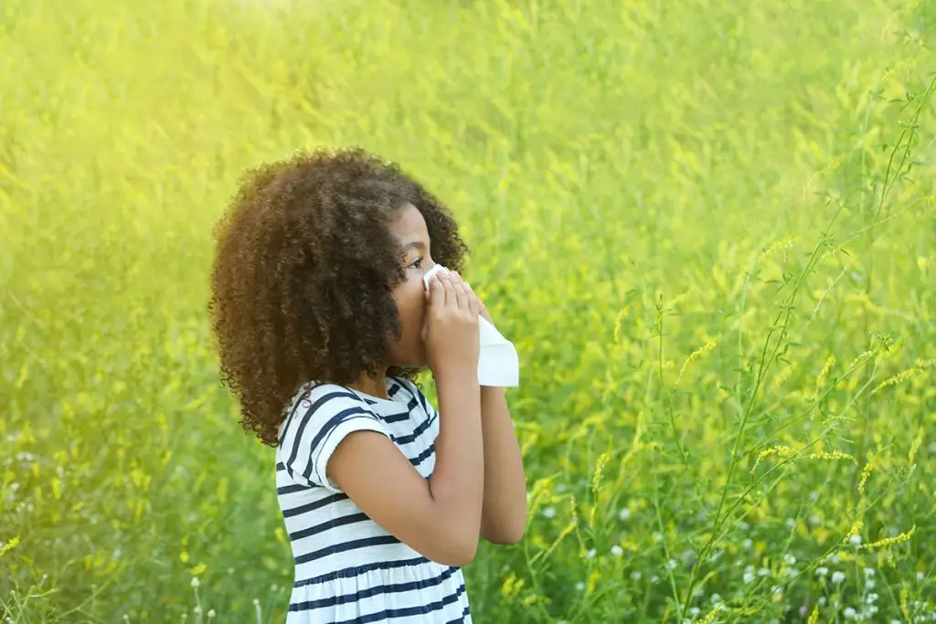 Young African American girl blowing nose in springtime field
