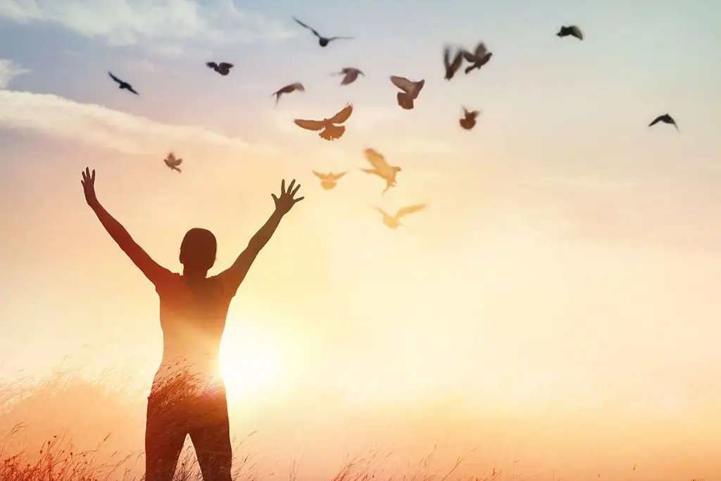 Woman outside with hands up to the sky as she frees herself from stress
