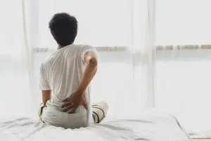 Man sitting on bad and touching his lower back