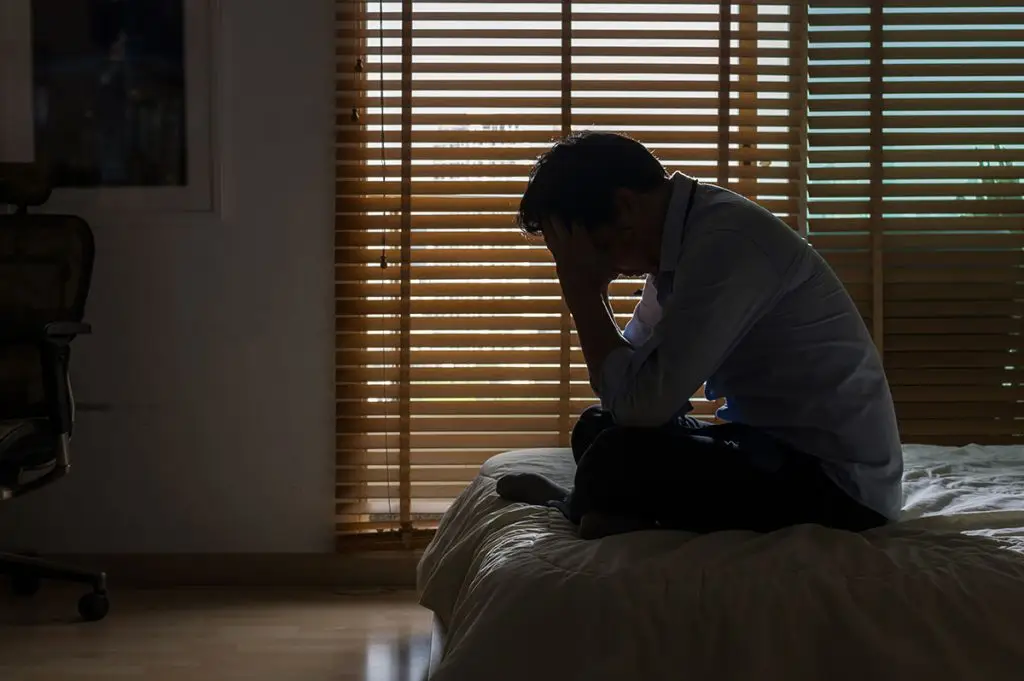 Business man sitting on bed in dark room with head in his hands
