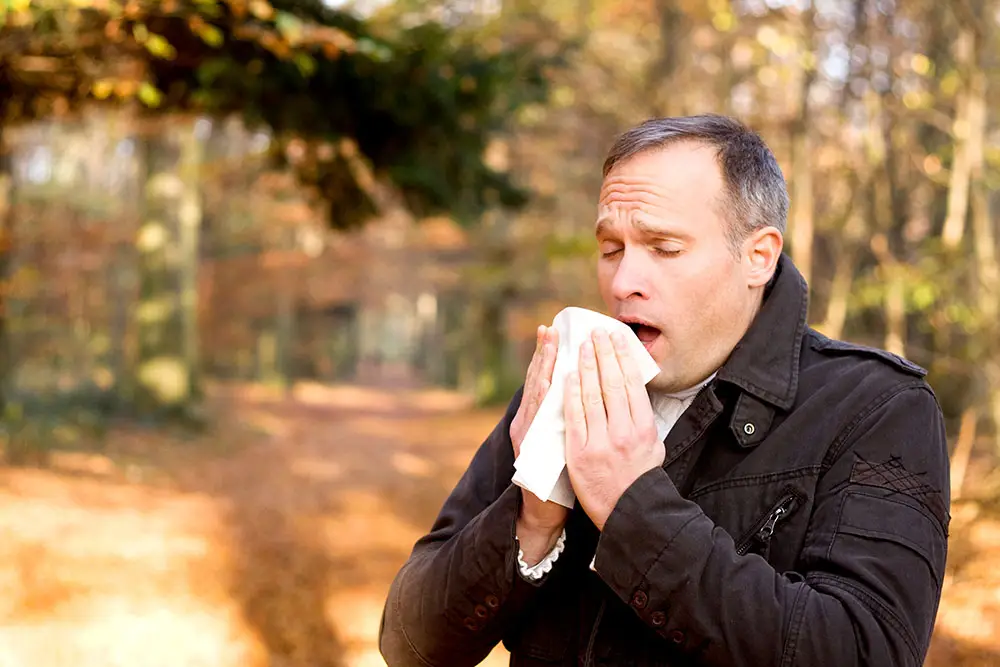 Man walking outside in the fall and sneezing into a handkerchief