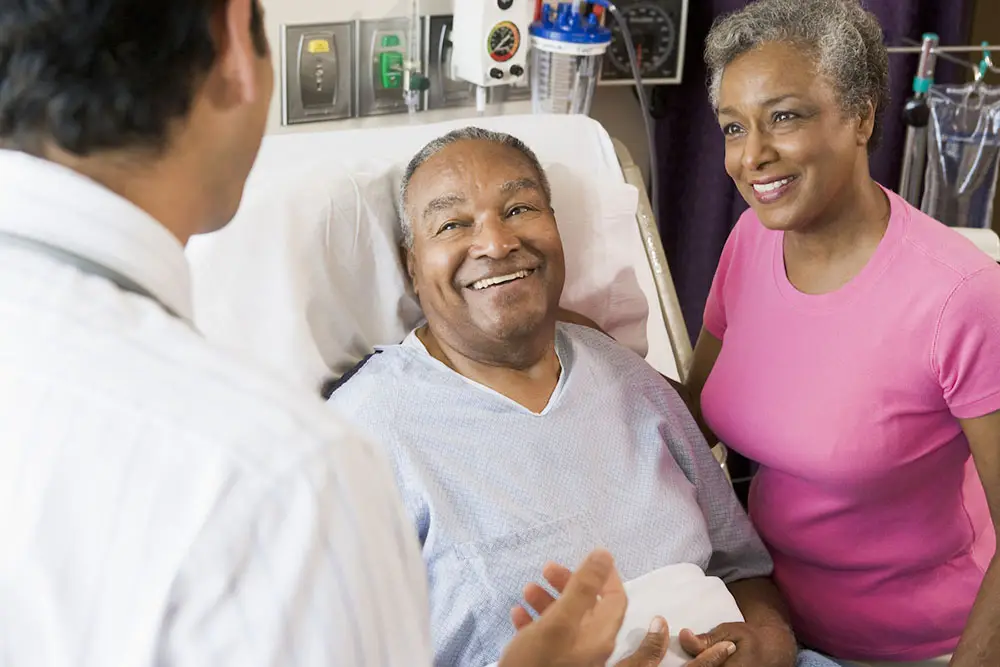 Man in hospital bed talking to his provider with his wife at his side