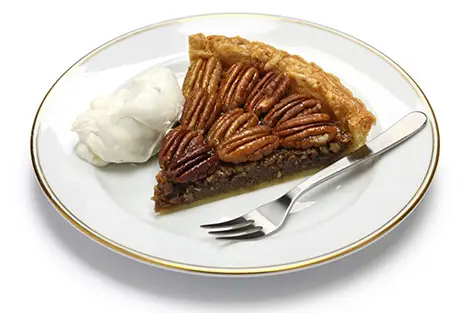 Holiday slice of pecan pie on plate with a fork and side of cream
