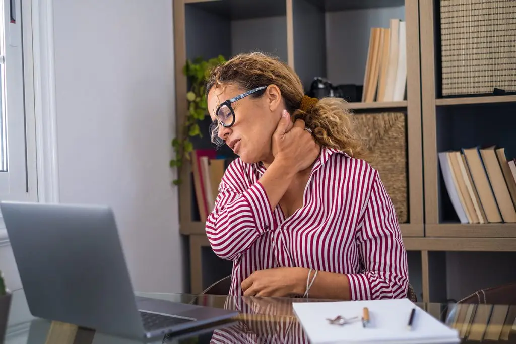 Woman with pinched nerve in neck sitting at the computer