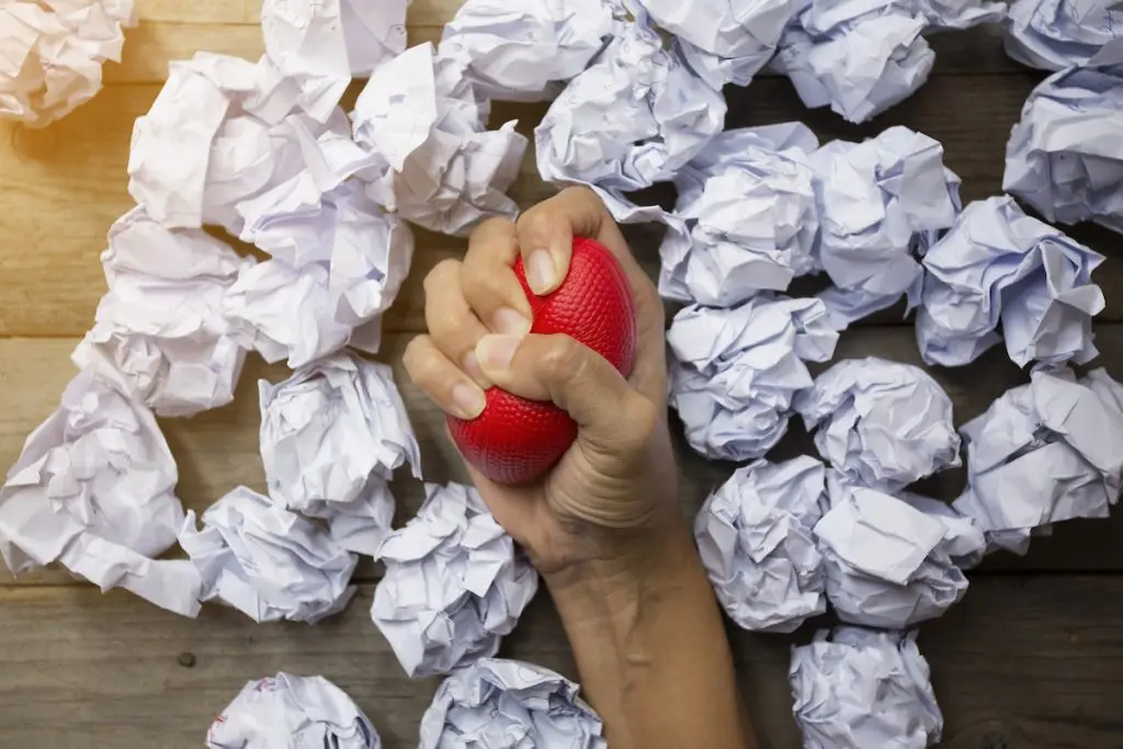 Person squeezing stress ball surrounded by paper balls