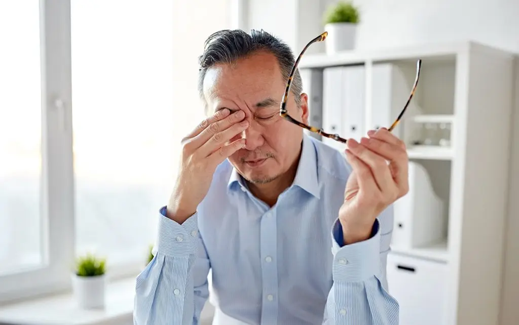 Older man taking off glasses and rubbing eyes sleepily
