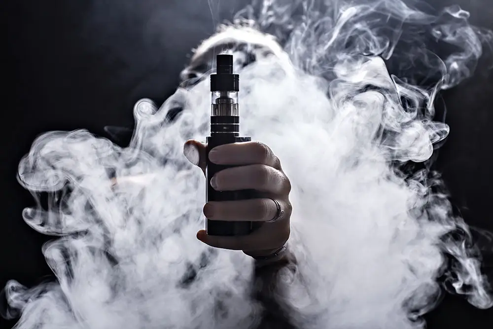 Hand holding e-cigarette vape as vapor swirls around it