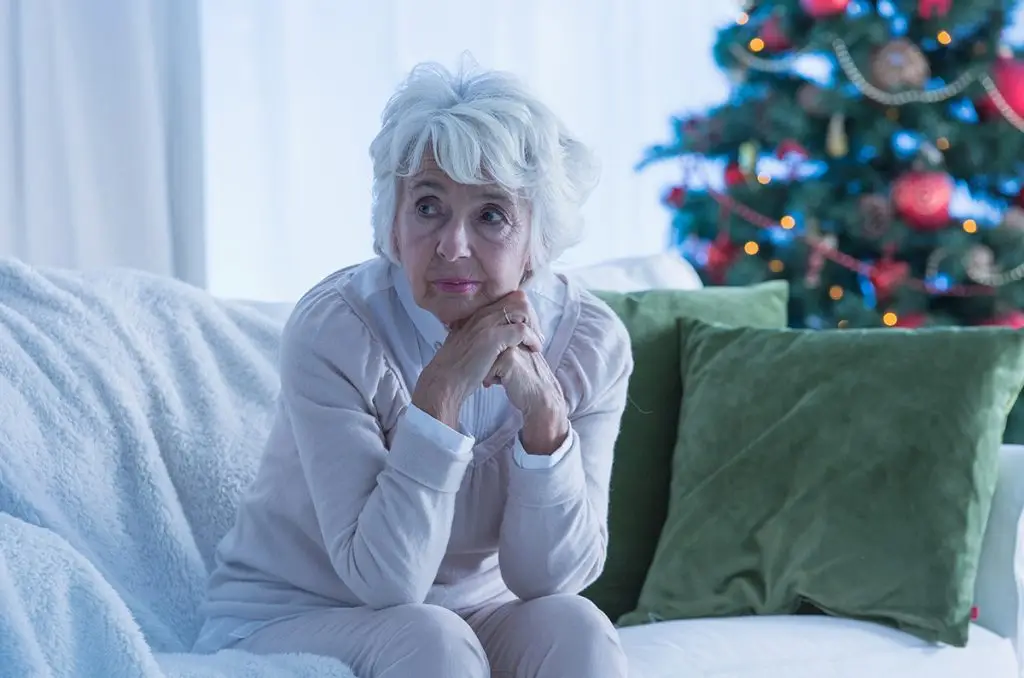 Older woman sitting alone on sofa and feeling sad during the holidays