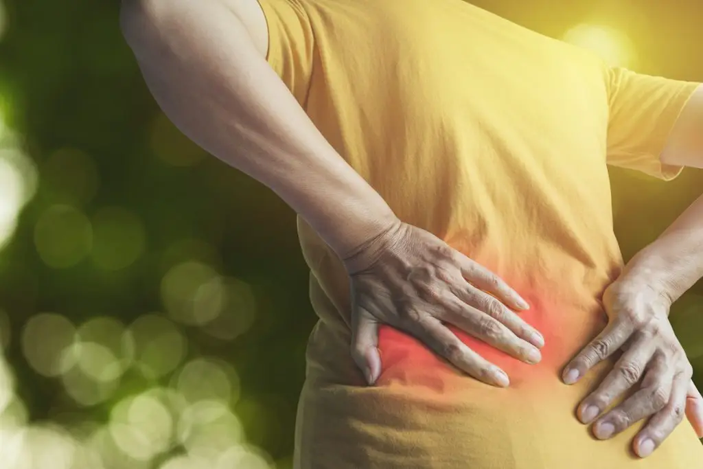 Woman's hands reaching around to touch her lower back that's in pain