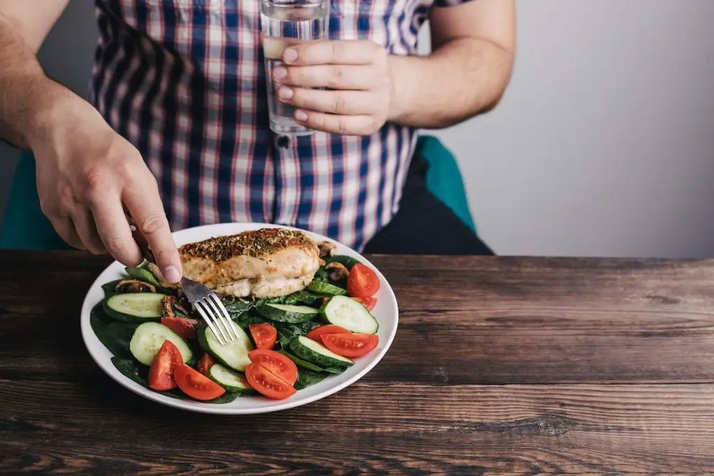 Larger man drinking water and eating a salad with grilled chicken