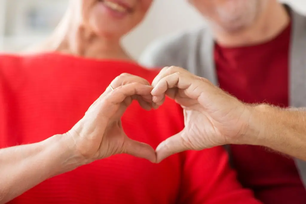 Older couple making a heart shape with their hands.